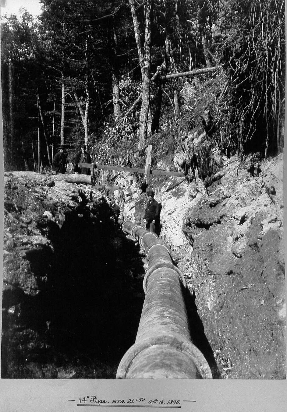 Man in trench with pipe and two men observing pipe
